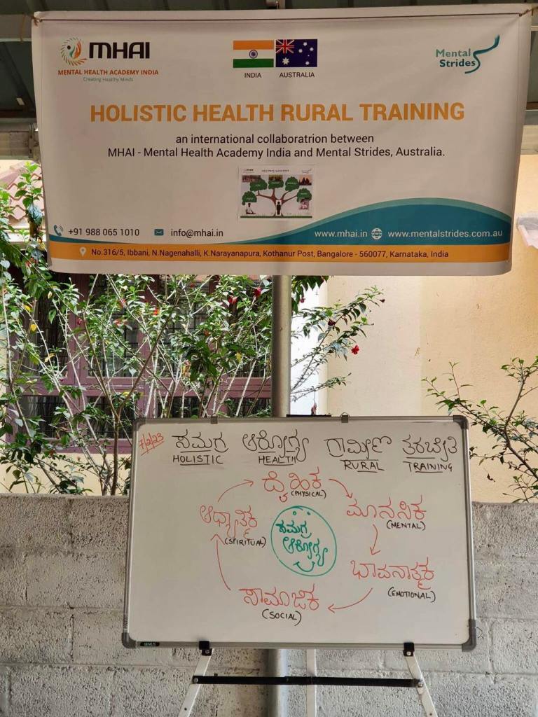 A Holistic Health training banner hangs above a whiteboard which introduces the training module to participants as part of the Mental Strides and Mental Health Academy India international partnership.