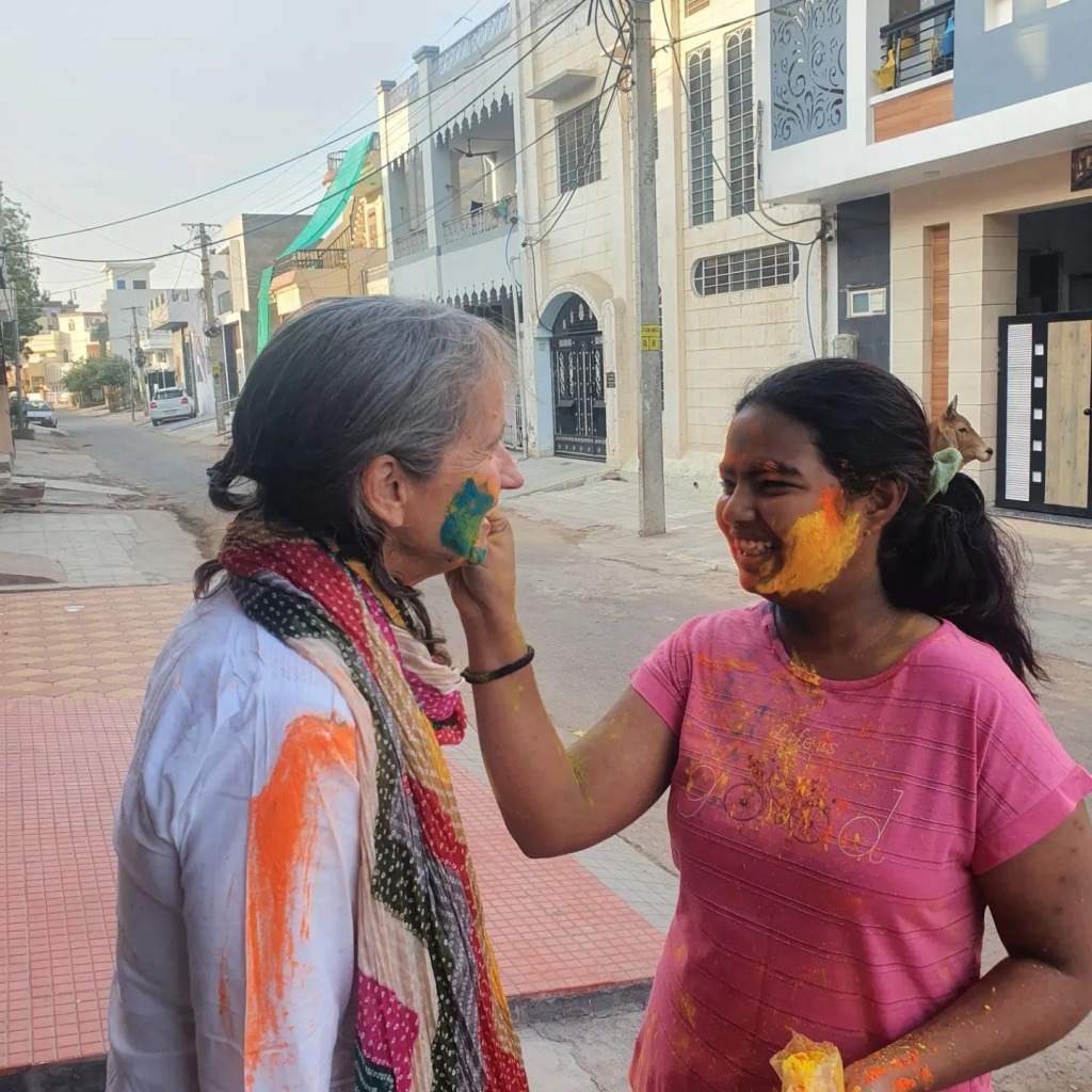 A young Indian girl, covered in paint, applied paint to the face of a Caucasian woman as part of The Fesitval of Colours.