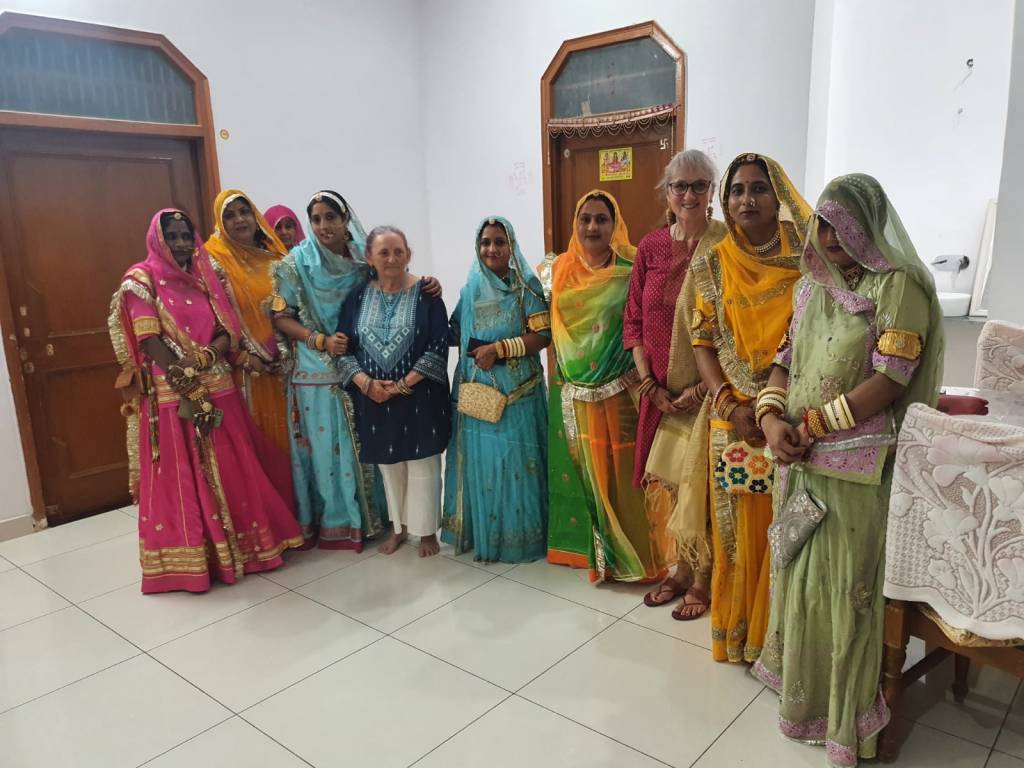 A large group of Indian women, dressed in colourful saris, pose for a photo as part of wedding festivities.