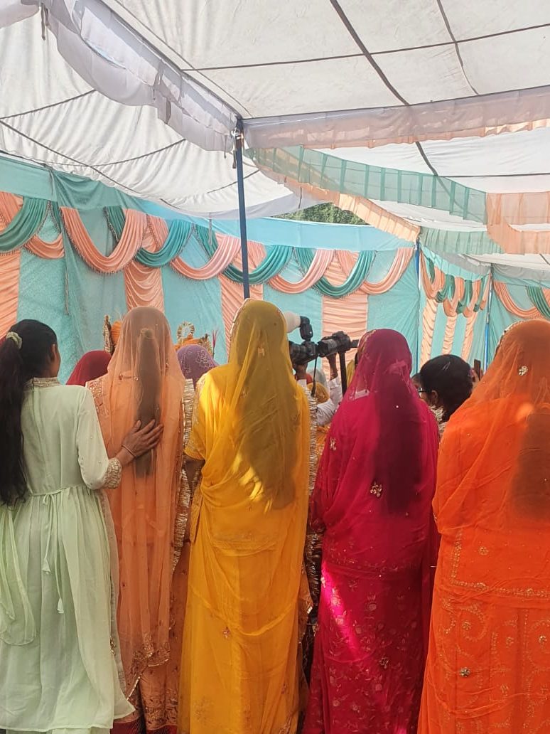 Five Indian women, dressed in colourful saris, watch the wedding festivities.