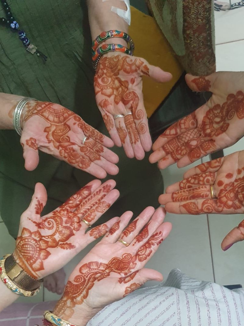 Three women hold out their hands, showing henna tattoos as part of Indian wedding celebrations. 