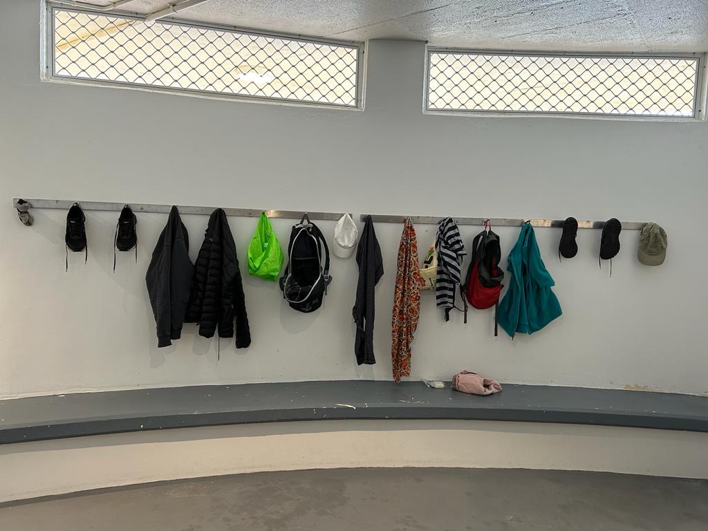 Clothes hanging on pegs on a white wall in a swimming pool changroom by the sea.